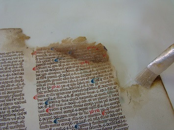 Le coin supérieur droit du document est déchiré et lacunaire. Un pinceau est utilisé dans le cadre de la restauration.