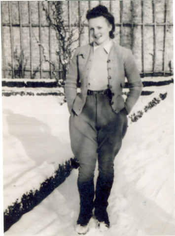 Marie Cauchy est dehors dans la neige en tenue civile avec un pantalon maintenu par une ceinture et une veste.