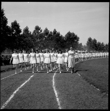 Des dizaines d'élèves de l'école ménagères défilent en rang comme des soldats sur la piste d'athlétisme du stade du Plateau de la Société Métallurgique de Normandie avec à leur tête l'institutrice.