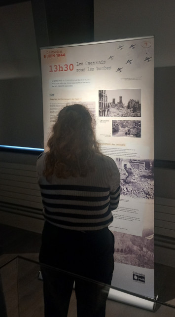Photographie montrant une visiteuse lisant le panneau de l'exposition consacré aux bombardements de Caen