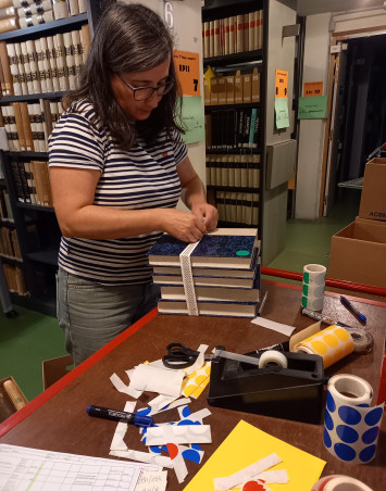 Une archiviste met une sangle sur plusieurs volumes.