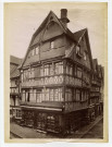 49 - Maisons à pans de bois et magasin de chaussures "Aux marques de fabriques" situés à un carrefour à Lisieux, par Paul Robert et Médéric Mieusement (édition)