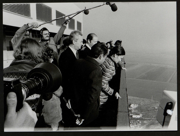 Simone Veil suivie par des journalistes se penche sur la rembarde du haut de la tour du CHU de Caen.