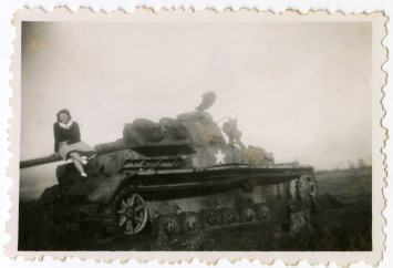Une jeune fille pose pour la photographie assise sur le canon d'un char d'assaut détruit.