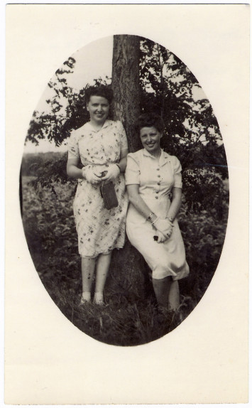 Les deux sont devant un arbre en robe avec des gants blancs.