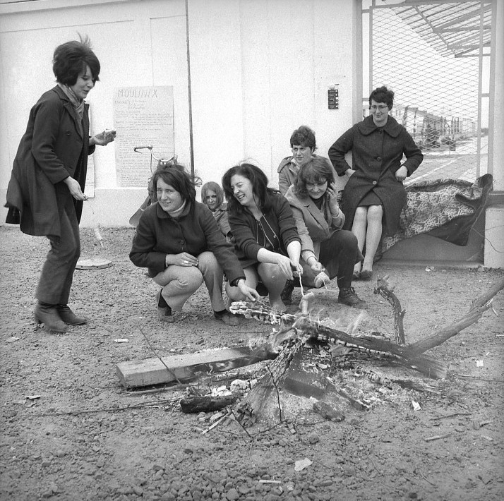 Trois femmes alimentent un feu de camp devant l'entrée de l'usine en grève.