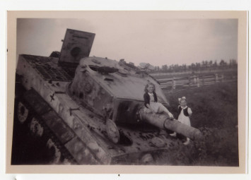 Deux jeunes filles bien habillées posent pour la photographie. L'une d'entre elles est assise sur le canon du char d'assaut bloqué dans un fossé.