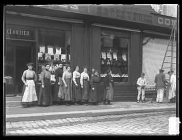 Il s'agit d'un magasin de cloutier. Les femmes qui y sont employées posent devant l'entrée du magasin.